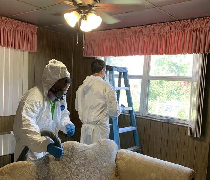 SERVPRO team members cleaning the floors in the room with pink and white curtains. 