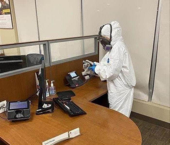 Person in PPE cleaning next to a desk.