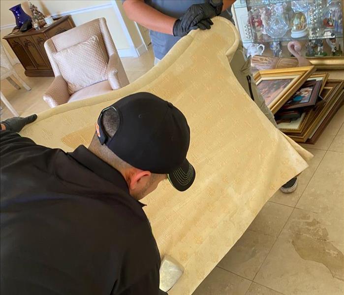 Two men cleaning a couch with a vacuum. 