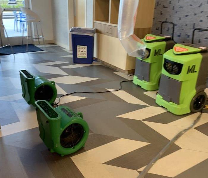 Grey and white flooring covered in green air movers and air scrubbers. 